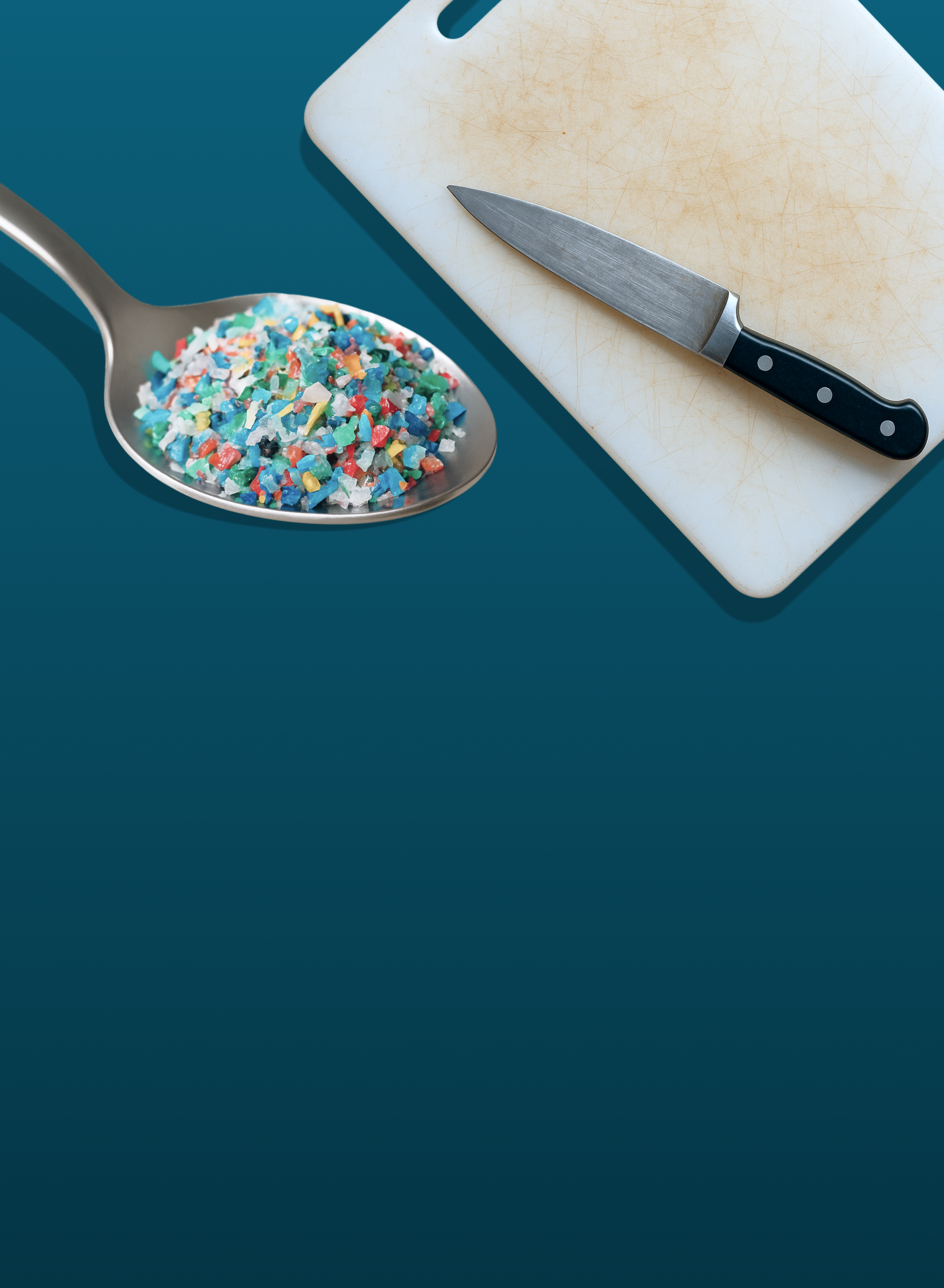 A spoon filled with colorful plastic fragments sits next to a well-used cutting board and a kitchen knife on a blue background.