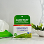 A box of Boiron Histaminum 30C Meltaway Pellets + Bonus Pack – Allergy Relief sits on a white table beside a tissue and a small potted plant. The packaging highlights homeopathic relief for hay fever symptoms, hives, and indoor or outdoor allergies with convenient meltaway pellets.