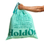 A hand holds a mint green HoldOn Bags Compostable Tall Kitchen Bag (13 gal, unscented) with motivational messages, promoting optimism and eco-responsibility. These plastic-free trash bags offer an environmentally friendly solution, shown against a clean white background.