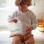 A young child with curly hair sits on a kitchen counter, looking down at a clear, freezer-safe HoldOn Bags Compostable Sandwich Bag filled with snacks. A bowl of fruit in the background highlights these food-safe kitchen essentials.