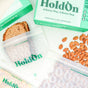 A sandwich in a HoldOn Bags Compostable Snack Bag—freezer safe and BPA-free—with loose almonds next to two empty HoldOn Bags and packaging, all on a white surface.