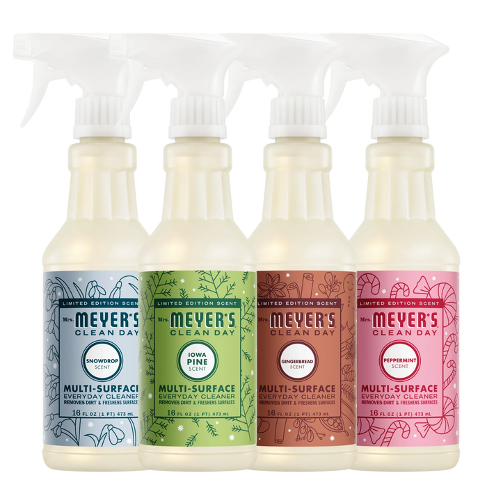 Four spray bottles of Mrs. Meyer’s Holiday Multi-Surface Cleaner Collection in holiday scents: blue Snowdrop, green Iowa Pine, brown Gingerbread, and red Peppermint, each featuring a garden-inspired scent.