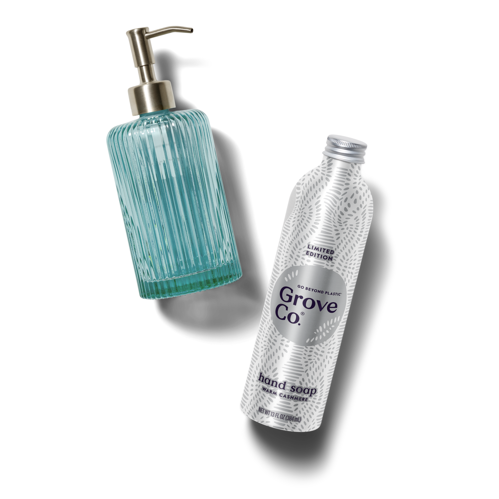 A ribbed blue glass soap dispenser with a metallic pump is next to a silver refill bottle labeled Grove Co. hand soap on a white background.