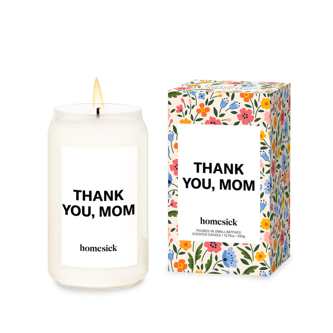 A lit Homesick Thank You, Mom Candle made from natural soy wax sits beside a matching floral box, both displaying the same heartfelt message.