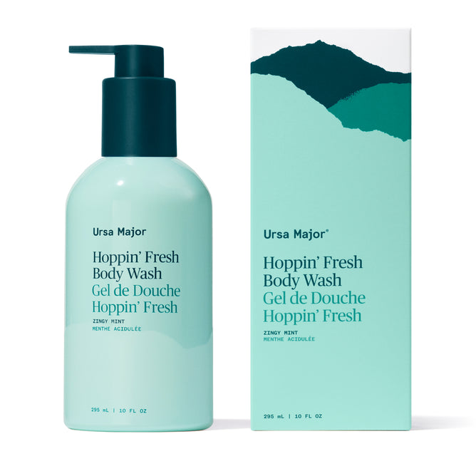 A light blue Ursa Major Hoppin' Fresh Body Wash with a pump sits beside its matching box, both featuring teal and dark green text, mountain graphics, and notes of peppermint and eucalyptus. The formula is sulfate-free.