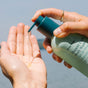 A person pumps Ursa Major Hoppin' Fresh Body Wash onto their palm, with a blurred outdoor background in view.