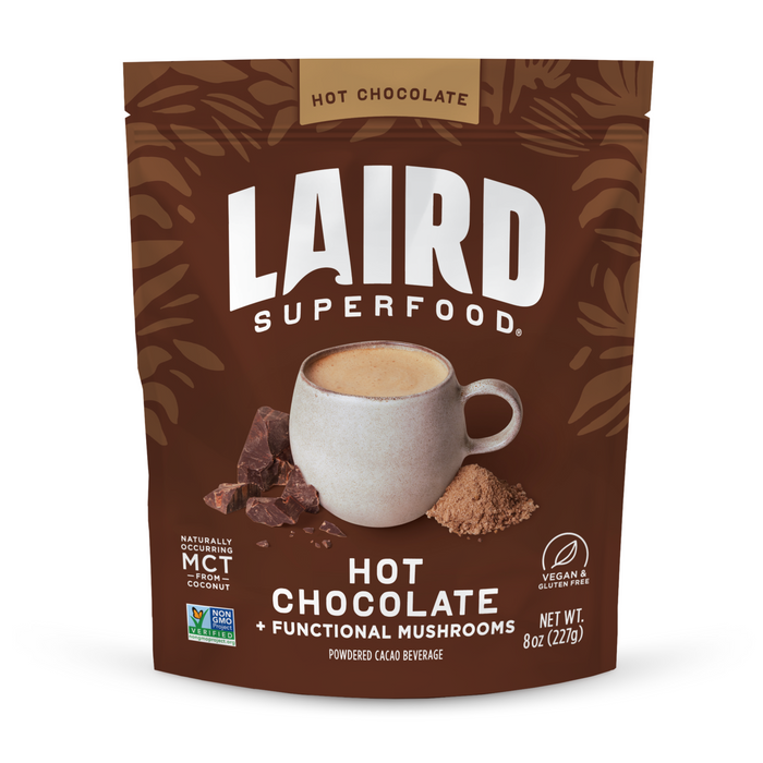 A brown pouch of Laird Superfood Hot Chocolate displays a mug of hot chocolate, chocolate pieces, and cocoa powder, highlighting its vegan, gluten-free, and non-GMO certifications.