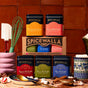 The Spicewalla Deluxe Hot Chocolate - Peppermint tin sits among kitchen utensils and spices against a tiled backdrop, showcasing its festive packaging in a cozy setting.