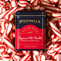 A tin of Spicewalla Deluxe Hot Chocolate - Peppermint, made with Guittard cocoa, sits amid peppermint candies. Its black and red tin has gold accents—a festive touch for holiday hot chocolate lovers.