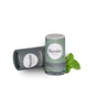 A green cylinder of Humble Brands Lip Balm - Paperboard stands upright with its cap beside it. Fresh mint at the base hints at its peppermint flavor, and the white background highlights this organic product.