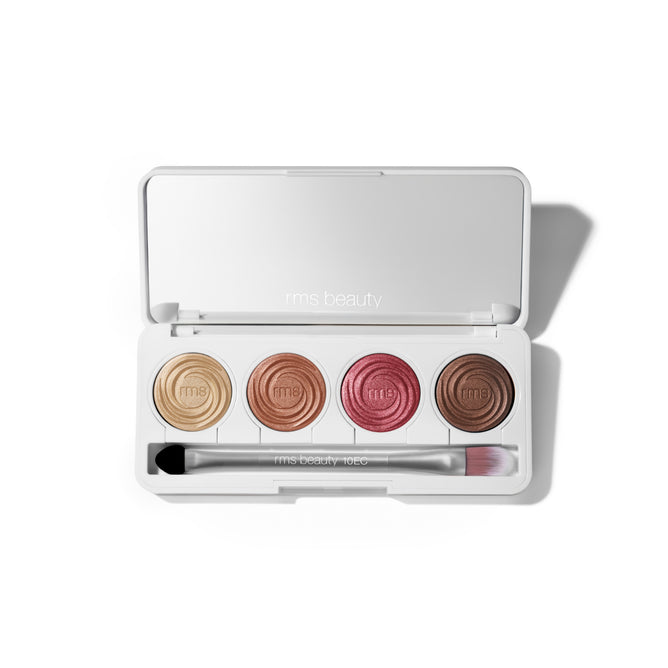 An open RMS Beauty ReDimension Hydra Eyes Quartet, a white talc-free palette, shows four shimmery shades—gold, bronze, rose, and brown—with a double-ended eyeshadow brush inside.
