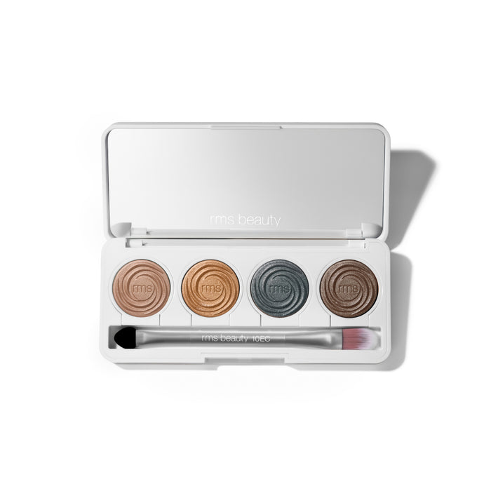 The open ReDimension Hydra Eyes Quartet by RMS Beauty shows a talc-free eyeshadow palette with four round pans—nude, gold, teal, and brown—plus a dual-ended makeup brush beneath them.