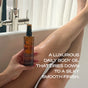 A person sits in a bathtub, holding Ember Wellness Hydrating Body Oil against their leg. Text on the image reads: Luxurious sandalwood-infused daily body oil dries to a silky smooth finish.