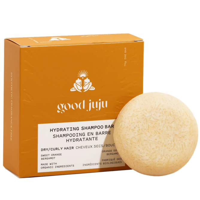 A round, beige organic Hydrating Shampoo Bar by Good Juju Body & Home sits in front of an orange box, offering frizz control for dry/curly hair with sweet orange and bergamot. Made with organic ingredients.
