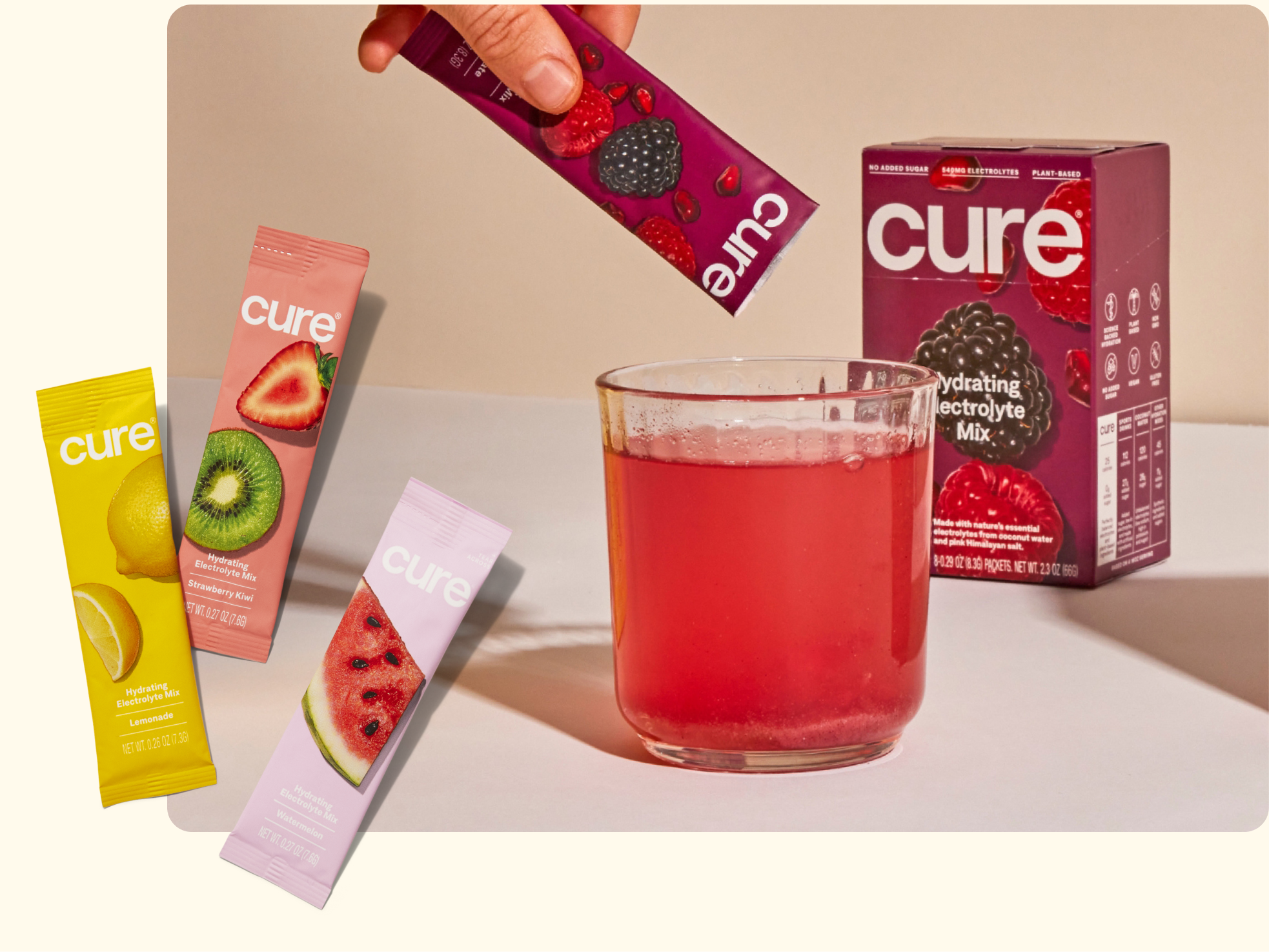A hand pours a berry-flavored Cure electrolyte mix into a glass of pink drink, with a Cure box behind it and three other flavored sticks (lemon, strawberry-kiwi, and watermelon) displayed on the left.