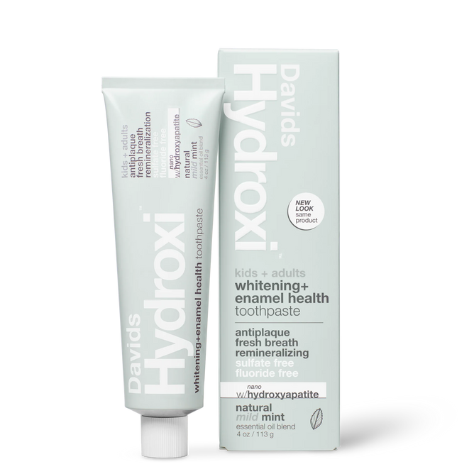 A tube and upright box of Davids Hydroxi Whitening + Enamel Health Toothpaste w/nano hydroxyapatite, labeled for natural whitening and enamel health for kids and adults. This fluoride-free toothpaste offers a mild mint flavor and the benefits of nano hydroxyapatite. The box stands upright beside the tube.