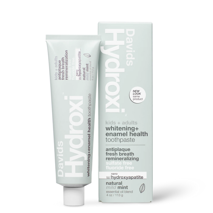 A tube and upright box of Davids Hydroxi Whitening + Enamel Health Toothpaste w/nano hydroxyapatite, labeled for natural whitening and enamel health for kids and adults. This fluoride-free toothpaste offers a mild mint flavor and the benefits of nano hydroxyapatite. The box stands upright beside the tube.