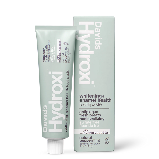 A tube and box of Davids Hydroxi™ Premium toothpaste - Whitening + Enamel Health w/nano-hydroxyapatite, a natural enamel health solution featuring nano-hydroxyapatite technology, in a refreshing natural peppermint flavor, are displayed upright against a white background. The light gray packaging with clean white and green text highlights this fluoride-free whitening toothpaste.
