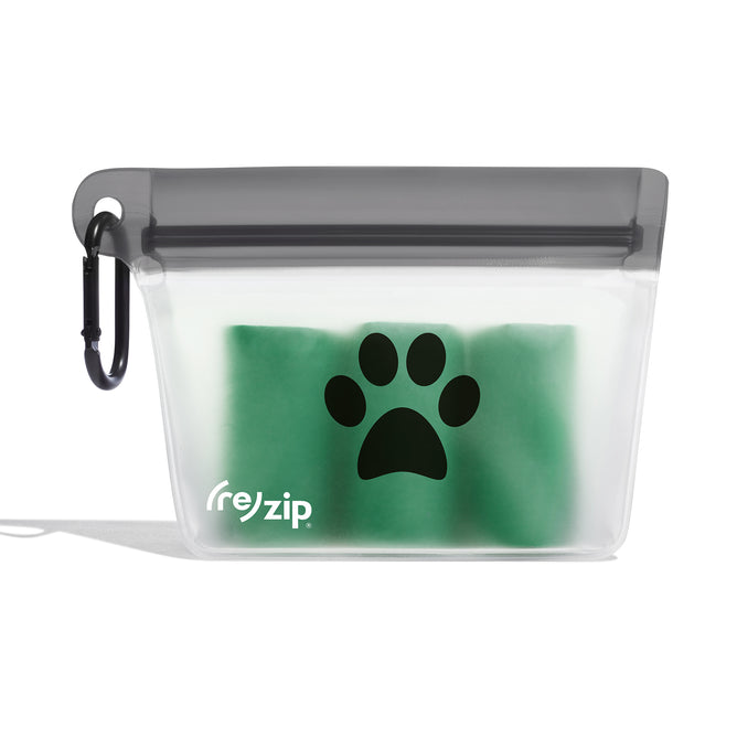 The (re)zip Take Me Too Pet Bag + Carabiner is a transparent, reusable zippered pouch with a black paw print and logo, green bags inside, and a carabiner—perfect as a leash accessory or dog treat bag for walks.