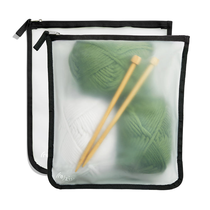The (re)zip Zippered Gallon Bag set includes two translucent, BPA-free PEVA pouches with black edges and zippers, holding green and white yarn balls. A reusable bag also contains wooden knitting needles, ideal for mobile knitters.