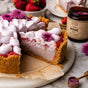 A slice of pink pie topped with whipped cream and purple flowers sits on marble next to strawberries, a jar of Anima Mundi ROSE, Love + Serenity* rose powder, and a spoonful of the pink powder for emotional balance.