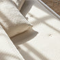 A close-up of a textured cream-colored Avocado Green Mattress Eco Organic Kids Mattress and pillow, with sunlight streaming through a window and casting soft shadows across the surface.