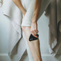 A person uses a KOA + ROY Large Black Obsidian Body Gua Sha Tool to massage their calf for lymphatic drainage. Theyre dressed in light-colored, ribbed leggings, and towels can be seen hanging in the background.