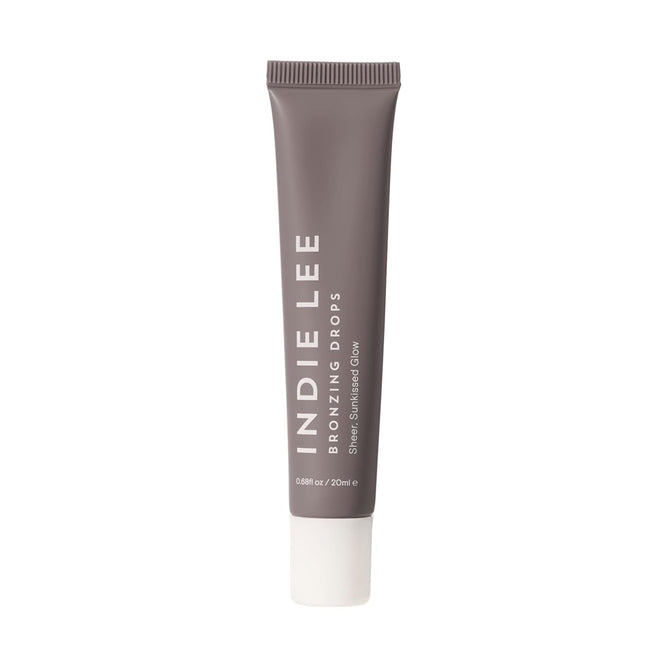 A taupe tube of Indie Lee Bronzing Drops with a white cap stands upright. The label says Indie Lee Bronzing Drops, a bronzing serum for a natural sun-kissed glow. The tube contains 20 ml (0.68 fl oz).