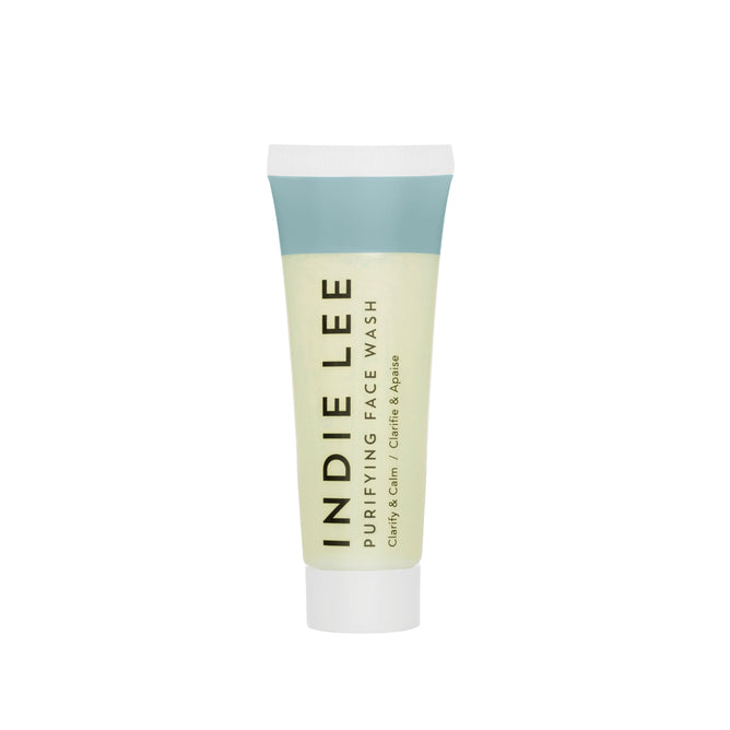A travel-size tube of Indie Lee Purifying Face Wash features a blue cap and label, with yellow-green hues highlighting Clarity, Calm, Chlorophyll, and Papaya—ideal for gentle makeup removal and refreshed skin.