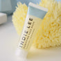 A tube of Indie Lee Purifying Face Wash - Travel, a natural cleanser with a light blue cap, sits in front of a yellow sea sponge on a soft, neutral background. The label reads Clarity & Calm | Clarifies & Apaises.