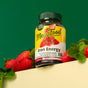 A bottle of MegaFood Iron Energy Gummies is displayed on a yellow surface with strawberries and green leaves, featuring strawberry flavor, vitamin B12, and energy support for teens and adults.