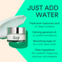 A jar of Dew Bomb Glowy Hydra-Milk Starter Kit by IZZY Zero Waste Beauty sits beside a cream smear on a teal and yellow background, highlighting hydrating hyaluronic acid, geranium oil, argan oil, and clean, paraben-free ingredients.