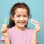 A smiling girl with wavy brown hair in a light purple shirt holds a yellow Jack N Jill Fairy Floss Floss Pick and its colorful package, promoting fun dental care for kids against a blue backdrop.