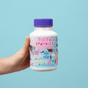 A hand holds a white bottle of Jack N Jill Tooth Sparkles Chewable Teeth Cleaning Tablets with colorful graphics, a purple cap, and text highlighting calcium, vitamin D, xylitol, and teeth remineralization for kids. Blue background.