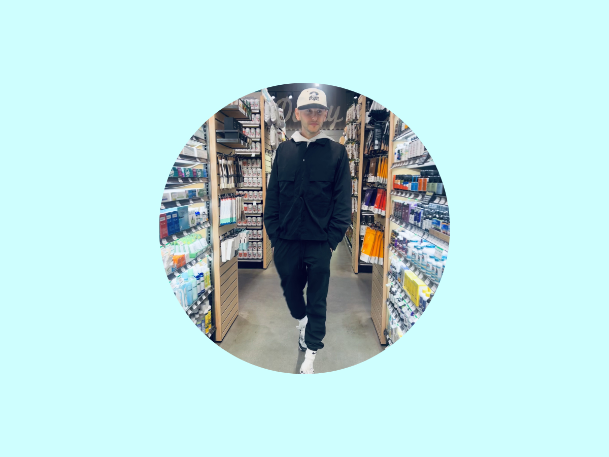 A person wearing a black jacket, black pants, white sneakers, and a white cap walks down an aisle in a store, surrounded by shelves stocked with various products. The image is centered in a circular frame on a light blue background.