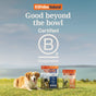 A happy dog relaxes on grass next to two K9 Feline Natural Dog Treat Protein Bites - Grain-Free, Air-Dried bags. A peaceful lake and blue sky are in the background. Text above: Good beyond the bowl. Certified B Corporation.