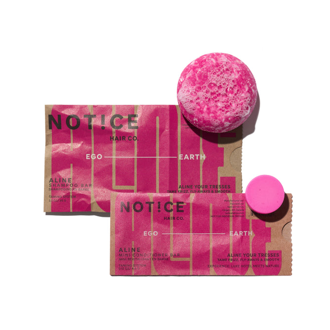 Two brown paper packages labeled NOTICE Hair Co. with bold pink branding are displayed on a white background. One package holds the ALINE Shampoo Bar, while the other contains the complimentary ALINE Mini Conditioner Bar, as part of the "Buy ALINE Shampoo Bar, Get ALINE Mini Conditioner Bar FREE" offer from NOTICE Hair Co. Both hair care products feature a vibrant pink color and are elegantly arranged side by side.