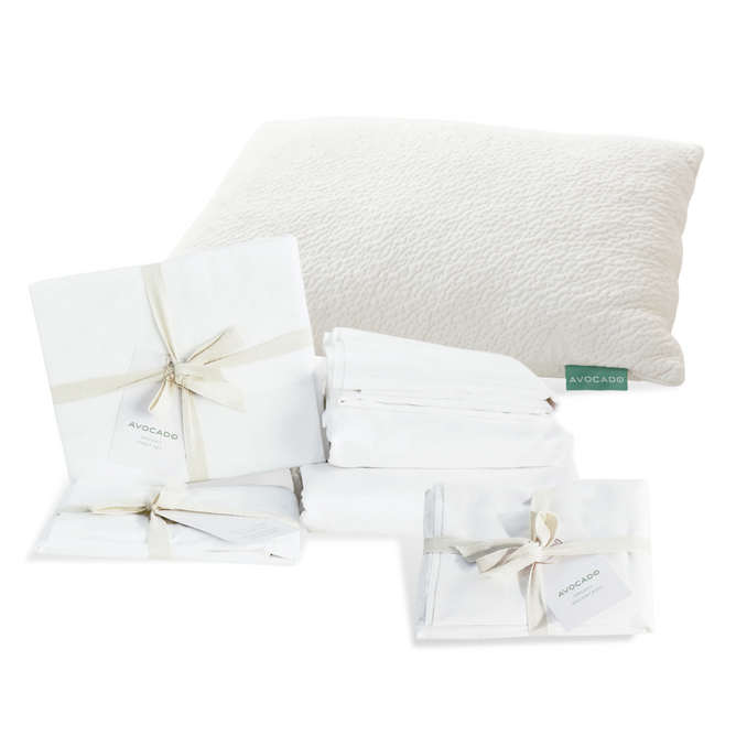 A fluffy white pillow with a green "Avocado" tag and neatly folded white sheets, bundled with ribbons and tags, are shown on a white background—Grove Collaborative’s Highest Impact Bedroom Swap Set: Everyday Sleep Essential.