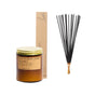 A hand-poured soy candle in an amber glass jar with a gold lid, labeled Saltwater Jasmine by P.F. Candle Co., is displayed with a rectangular box of Golden Coast Incense Sticks and black reed diffuser sticks—all part of the “Buy a Soy Candle, Get Golden Coast Incense Sticks Free” offer on a white background.