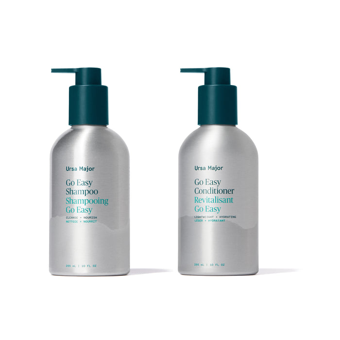Two silver pump bottles of Ursa Majors Go Easy Haircare Set—shampoo and conditioner—stand side by side, each featuring teal and blue text on white labels.