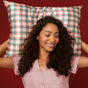 A woman with curly hair in a pink shirt smiles with eyes closed, enjoying beauty sleep while holding the Kitsch Standard Satin Pillowcase - Holiday Edition against a red background.