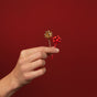 A hand holds two Metal Bobby Pins Gift Bow Set by Kitsch, one gold and one red, against a red background—fun festive hair accessories for the holidays.