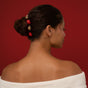 A woman with dark hair in a bun, styled with the Metal Bobby Pins Gift Bow Set from Kitsch, poses in an off-shoulder white top against a deep red background, showing her elegant profile.