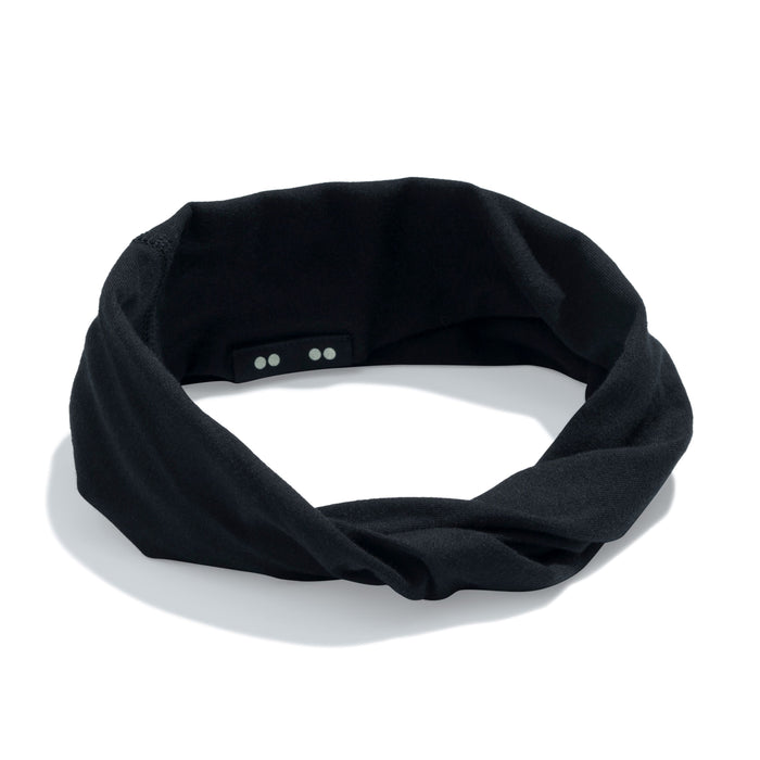 The KOOSHOO Organic Twist Headband is crafted from black organic cotton with a twist detail and circular shape, displayed on a white background. Inside, it features a small patch marked with three white dots.
