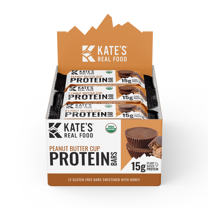 Kates Real Food Organic Protein Bar - Peanut Butter Cup display box offers 15g plant-based protein per bar, made with whole-food ingredients. The USDA organic, gluten-free box features images of chocolate bars and peanut butter cups.