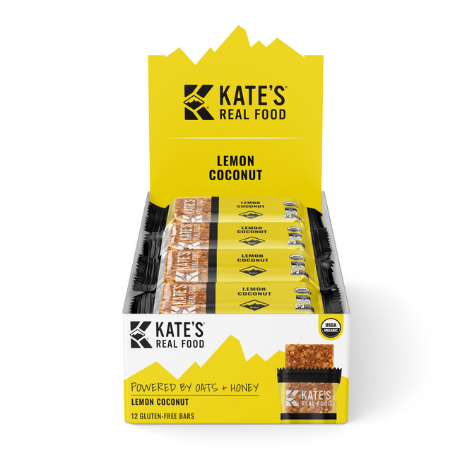 A vibrant yellow display box of Kate’s Real Food Organic Energy Bar - Lemon Coconut, containing 12 gluten-free bars made with organic oats—each bar individually wrapped with bold branding and clear product details.