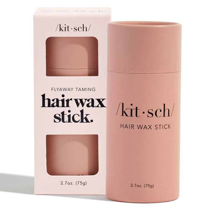 A pink cylinder and matching box for Kitschs Hair Wax Stick are shown, labeled as a vegan Flyaway Taming Hair Wax Stick. Offering a strong hold at 2.7 oz (75g), the modern, minimal packaging effectively tames frizz.