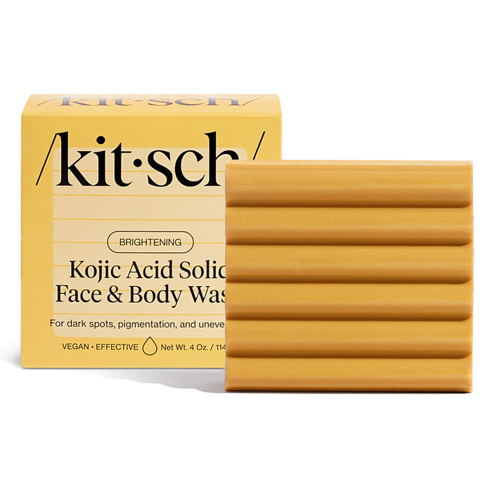 The image shows a yellow, ribbed-textured Kojic Acid Solid Face & Body Wash by Kitsch. Its 4 oz and promotes brightening to address dark spots and hyperpigmentation, effectively tackling uneven skin tones.
