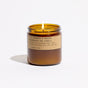 A lit amber jar candle with a tan label that reads "Large Concentrated Soy Candle" by P.F. Candle Co. and features additional product details. Hand-poured with soy wax, this candle is displayed against a white background.