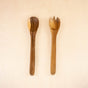 The LIKHA Acacia Essential Serving Set, featuring two Fair Trade utensils, is displayed side by side on a light wooden surface.